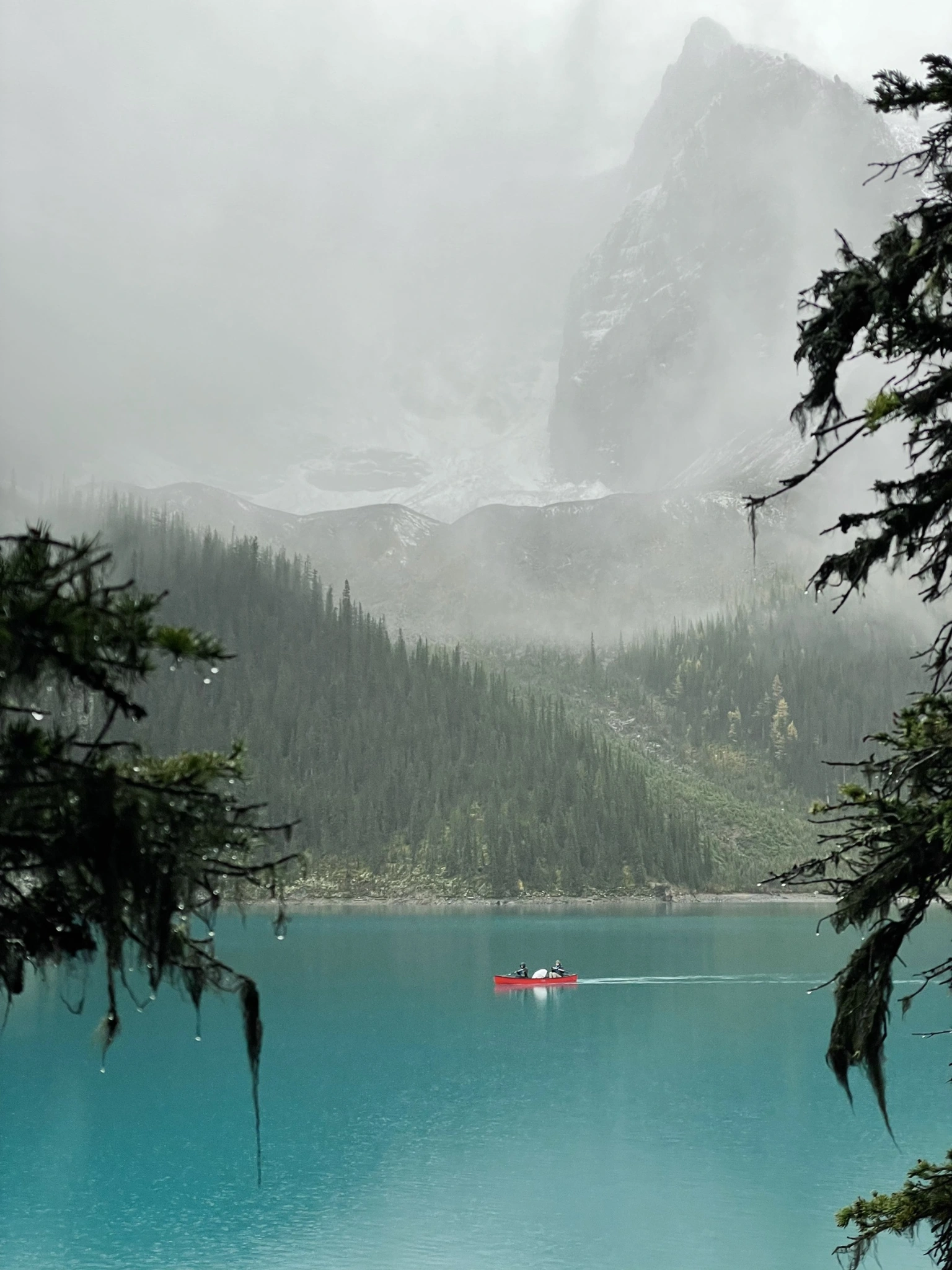 Moraine Lake in rain and mist, with a red canoe.